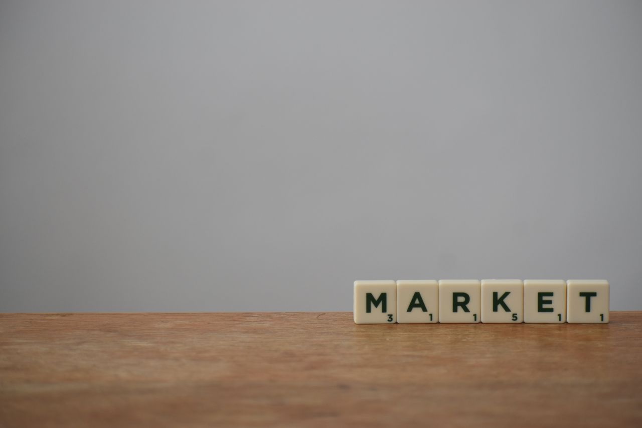 Tevékenységünk Scrabble tiles spelling 'Market' on a wooden table with a minimalist background.